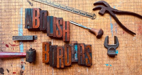 Carved woodcut that says "Abolish borders" and various tools.